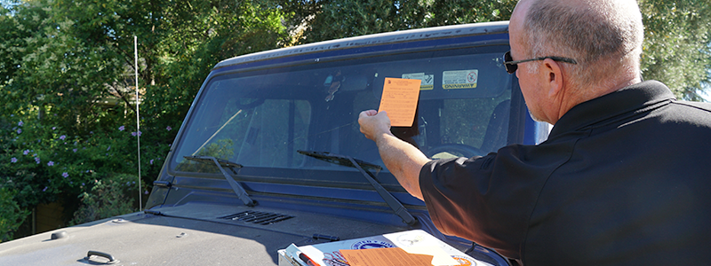 Code Enforcement photo of an officer placing an orange slip on a car windshield.