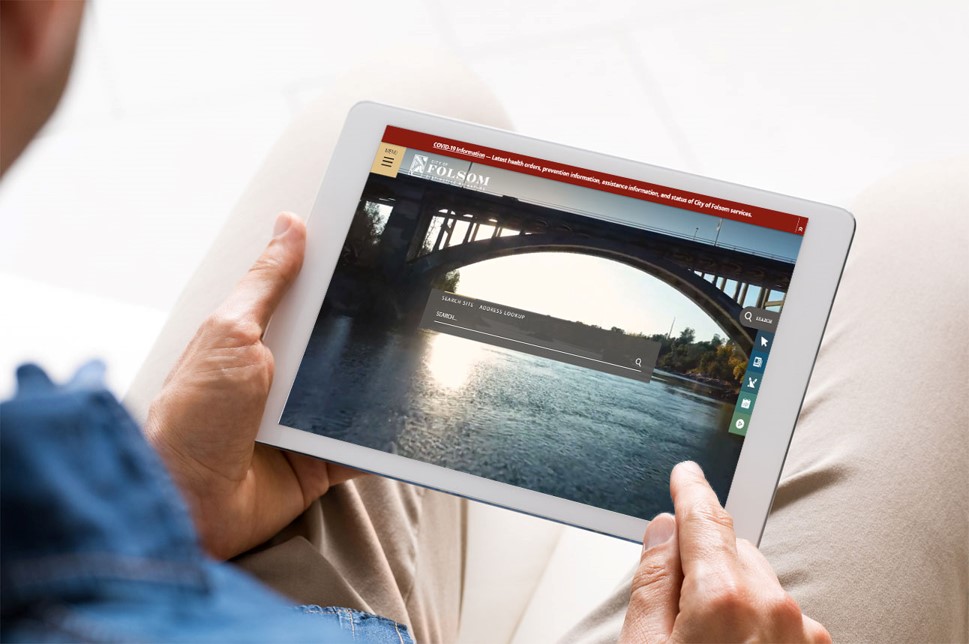 Stock image of a man wearing a blue shirt and beige pants, looking down at an iPad with the City of Folsom website home page on the screen