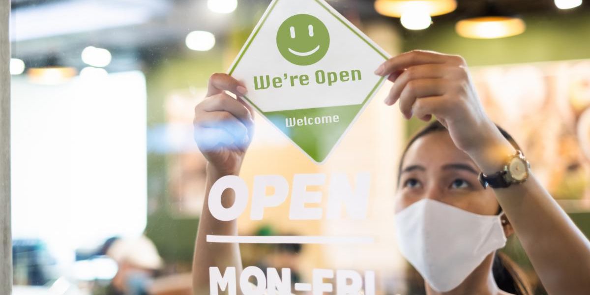 Getty Images of a worker placing an open sign on a glass door while wearing a mask