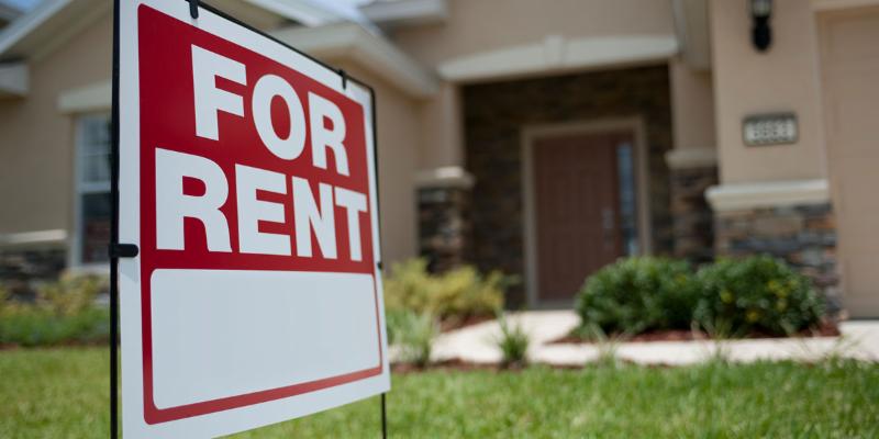 image of a for rent sign in front of a house with bushes and a green grassy front lawn