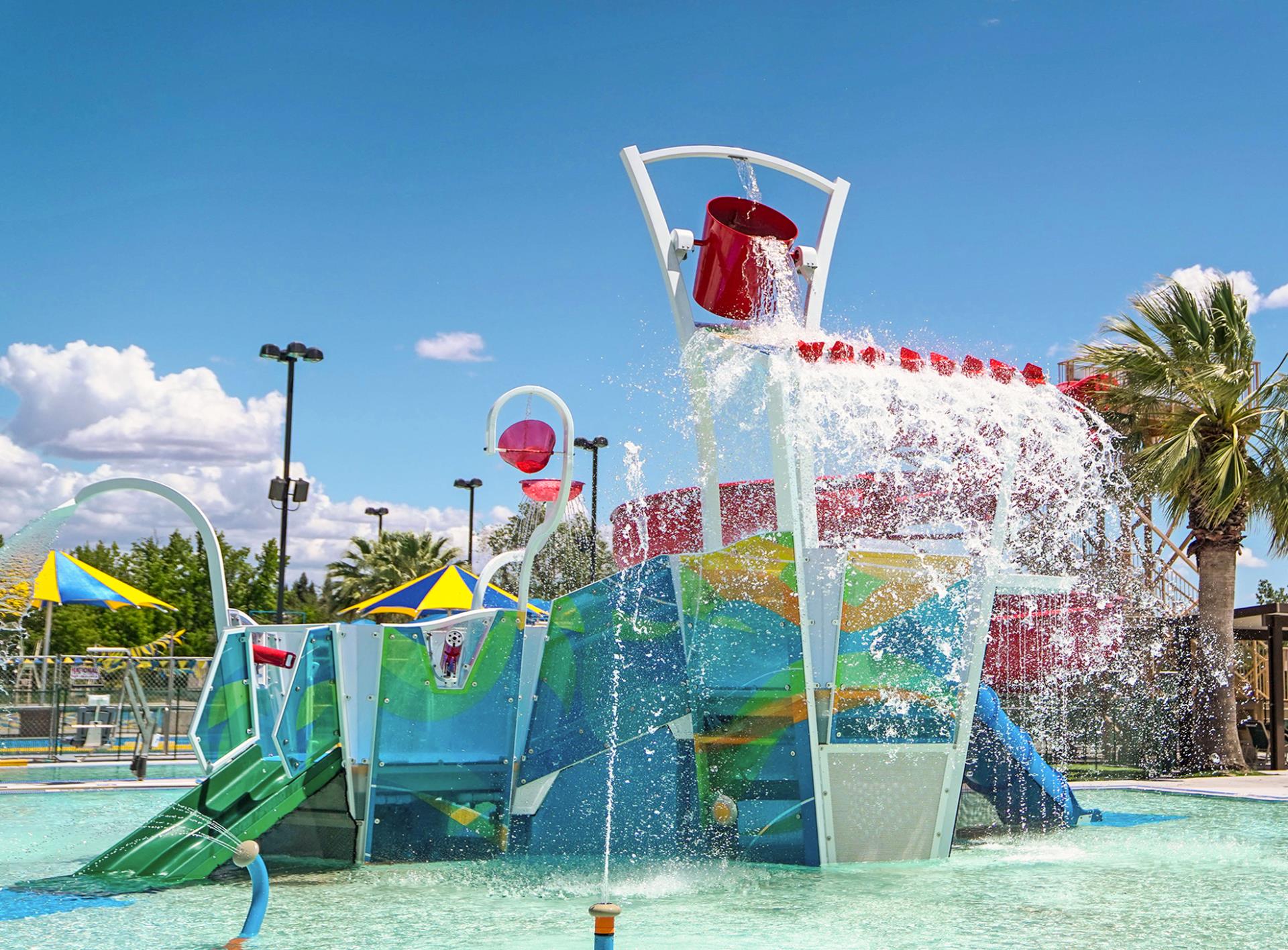 Photo of Steve Miklos Aquatic Center Play Structure with water features turned on, with a blue sky with clouds in the background