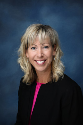 Community Development Director Pam Johns professional portrait headshot on a navy blue background wearing a hot pink top and a black jacket with pearl drop earrings