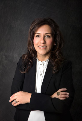 Councilmember Rosario Rodriguez portrait headshot on a dark gray background with a black blazer and a white top with a ruffled neckline with a silver necklace and wearing 3 rings
