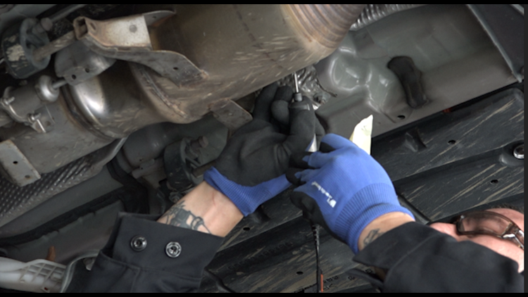 Mechanic's hands using etching tool to etch identifying information on catalytic converter
