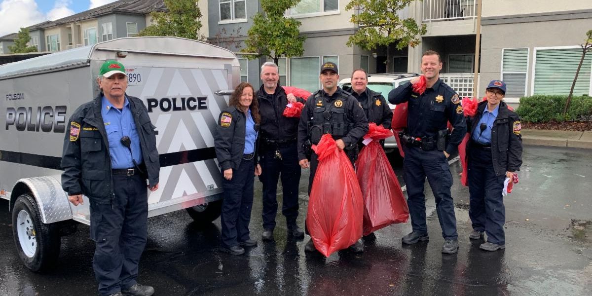 seven Folsom police and CAPS officers giving gifts in a neighborhood next to a Folsom Police hauling cart