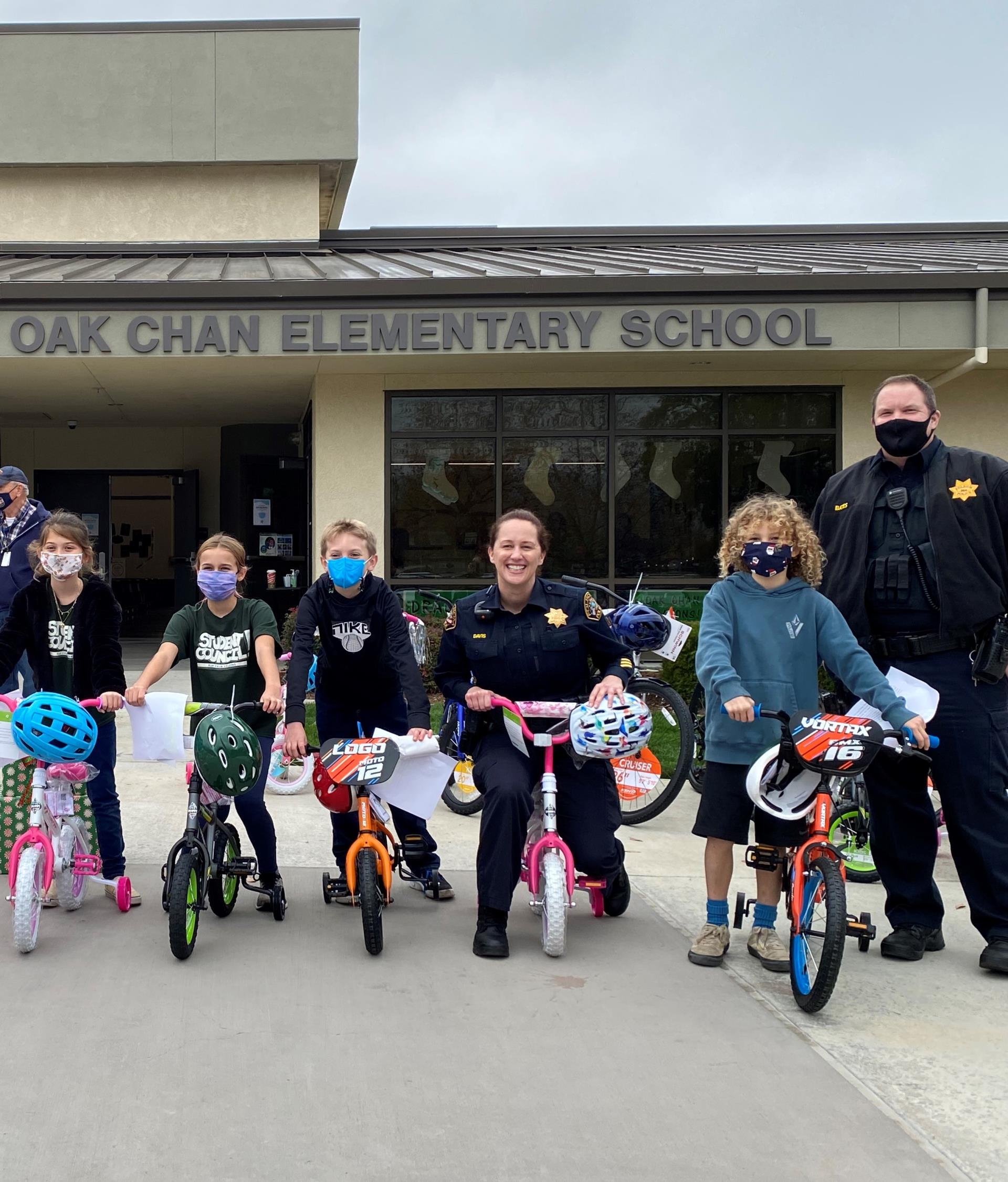 School Resource Officers at Oak Chan Elementary School with a group of students each holding a bicycle.