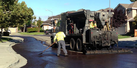 City Worker wearing a yellow reflective vest Repairing a Street with a Slurry Seal machine