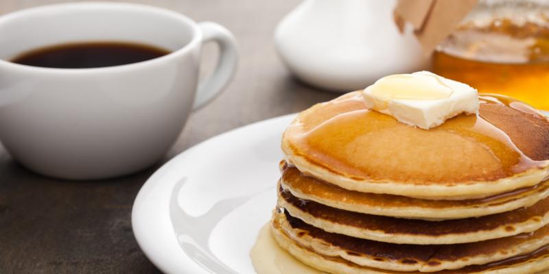 stack of pancakes on a plate next to a cup of coffee