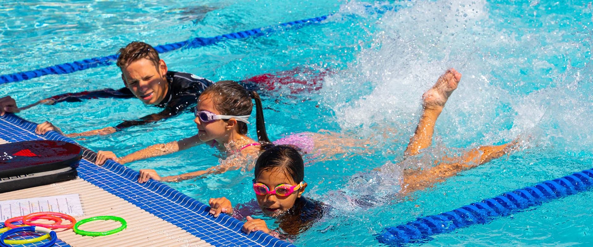 Swim lesson instructor and two youth swim lesson participants practicing kick strokes at the Steve Miklos Aquatic Center